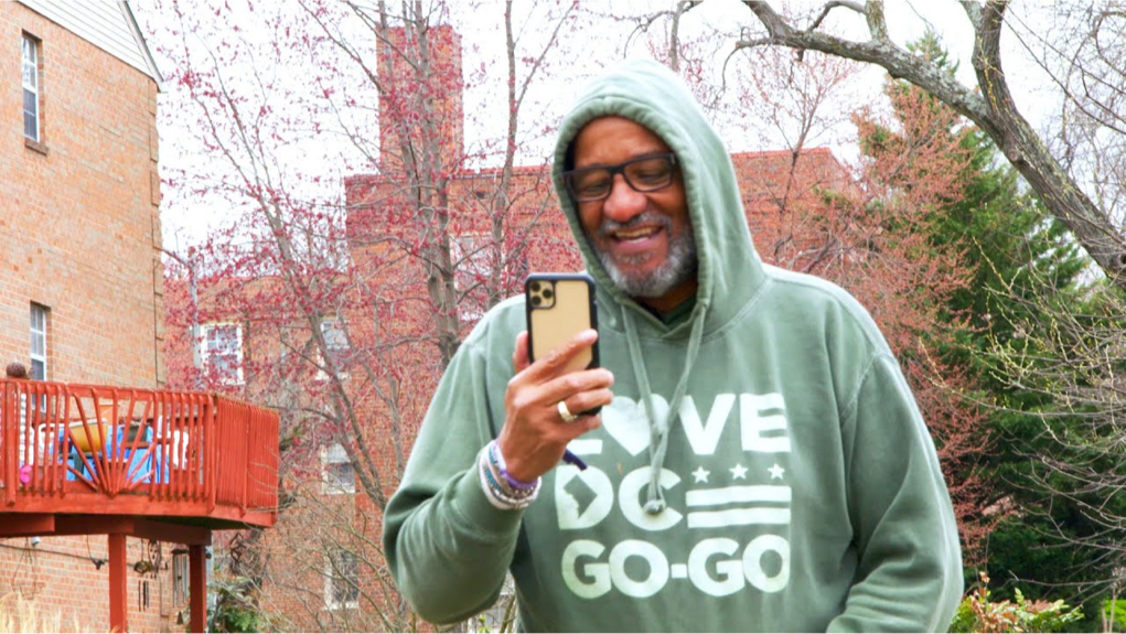 a man in a hooded sweatshirt smiling as he reads from his cell phone
