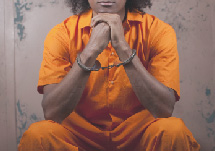 Image of woman sitting dow in a prison uniform with handcuffs
