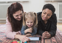 Two women reading with their young daughter