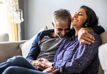 Man and woman sitting on a couch laughing while holding hands