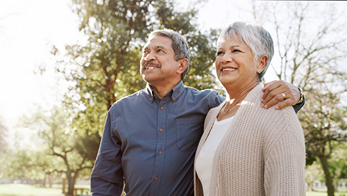 Senior Hispanic couple standing and smiling, with man having arm around woman's shoulders