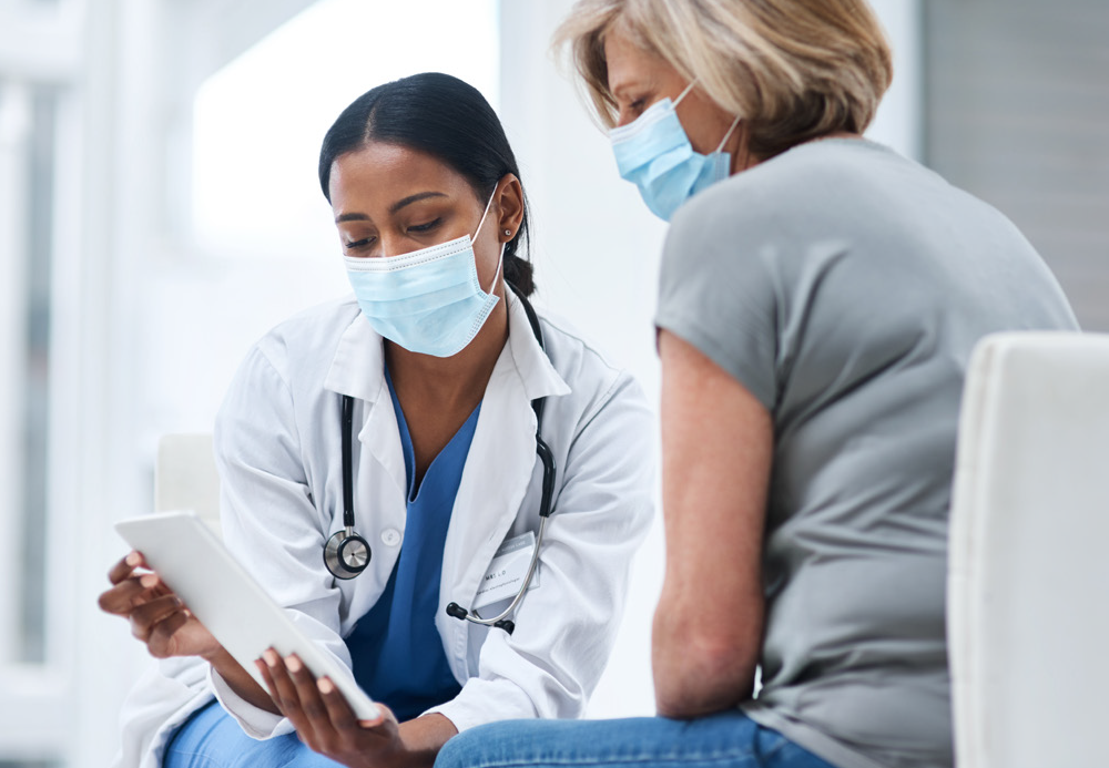 A healthcare woman holding a document, talking to a patient, both wearing masks