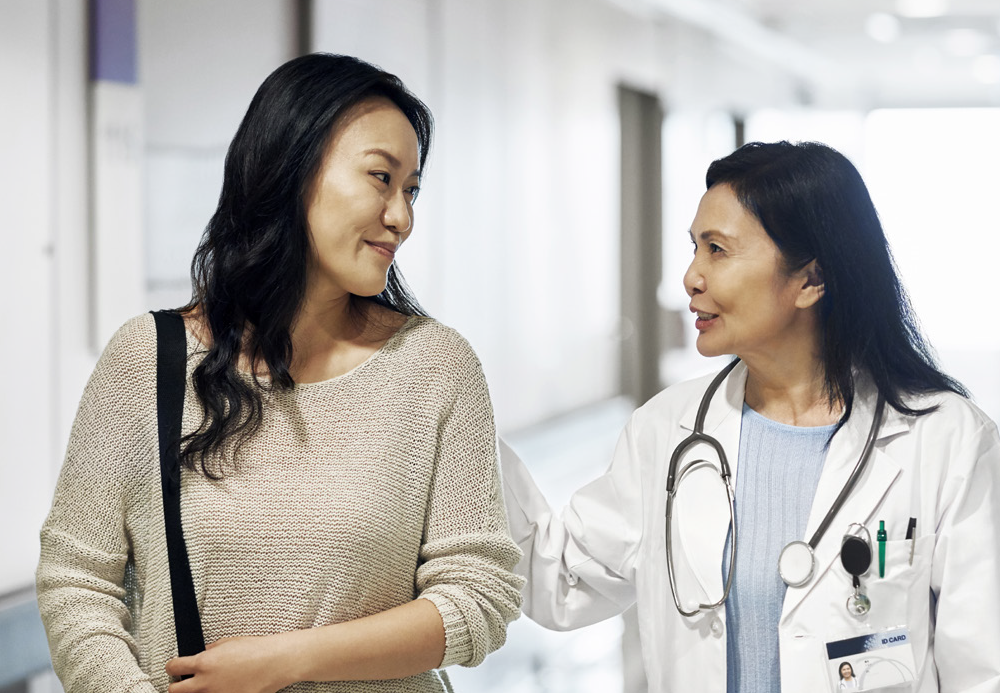 Female medical professional walking with female patient having a discussion and both smiling. 