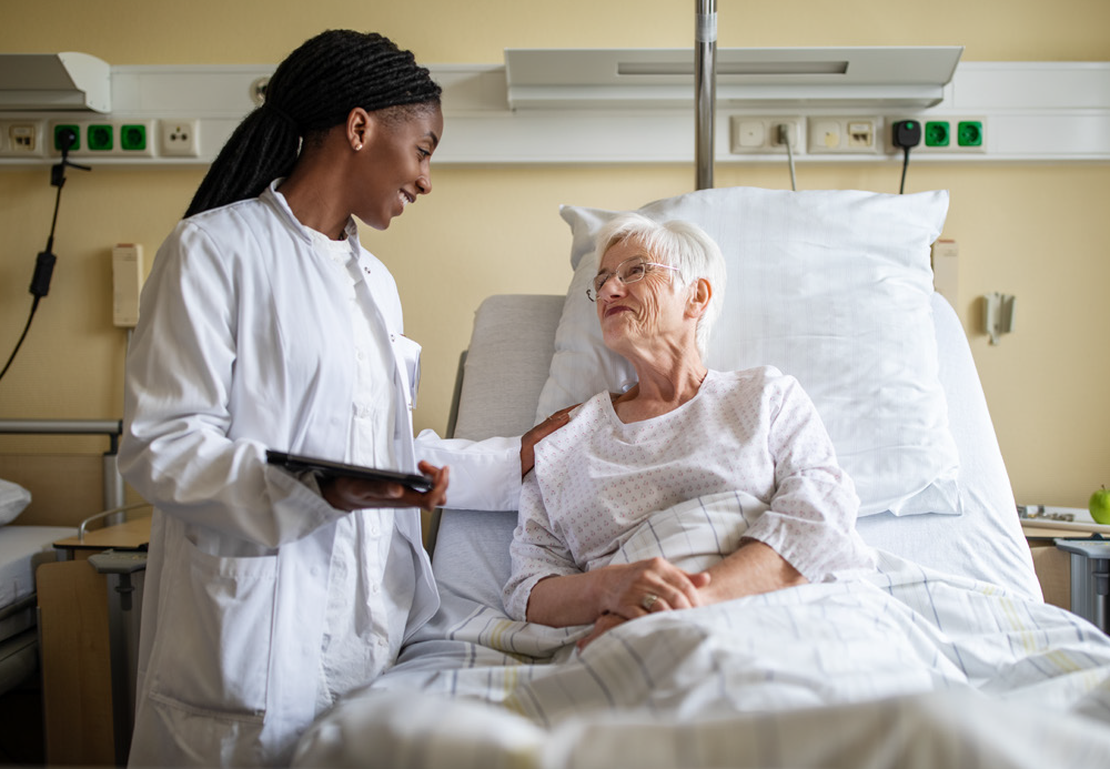 A medical woman standing and talking to an older woman in a bed