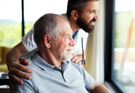 A medical man with his arms on the shoulders of an elderly gentleman whos sitting