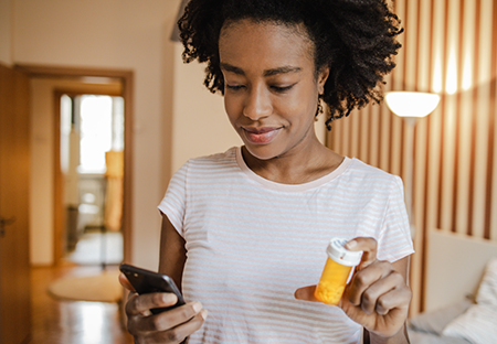 A young minority woman smiling and looking at her phone while holding a prescription bottle