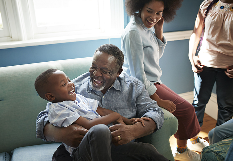 An older black man holding a laughing black child in his lap surrounded by his family