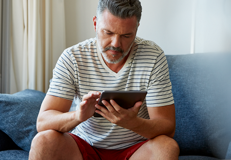 man sitting on couch attempting to use a tablet device