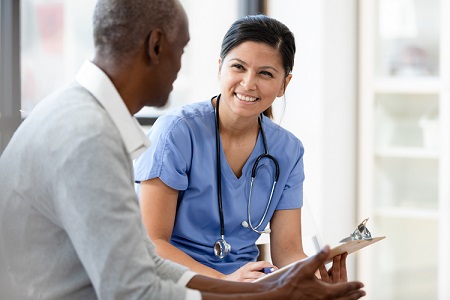 Female doctor wearing scrubs holding a clipboard and smiling at a patient