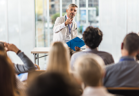Male Doctor sitting on a desk lecturing to a crowd