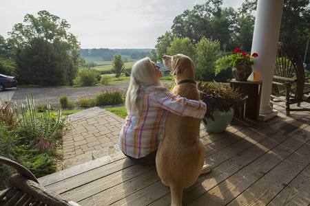 Woman sitting on a porch hugging a brown dog