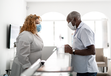 Masked receptionist and client talking with a desk and hand sanitizer between them