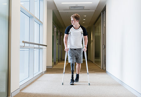 A young man with a leg prosthetic is walking on crutches