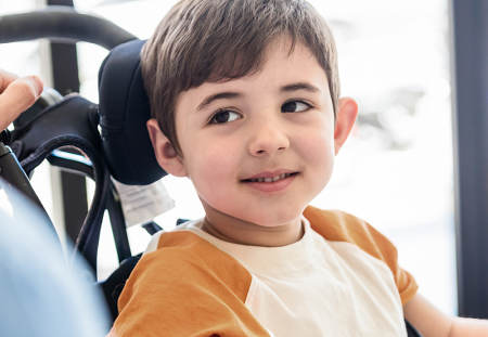 Boy in a wheelchair smiles at someone out of frame