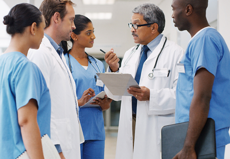 Group of medical professionals stand around a doctor who has a clipboard and is explaining something to his team