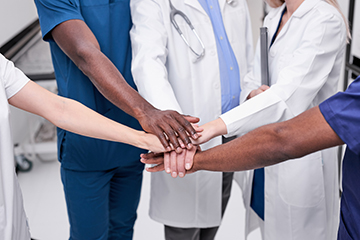 Image shoring a diverse group of four care providers with their hands stacked in the middle - go team! 