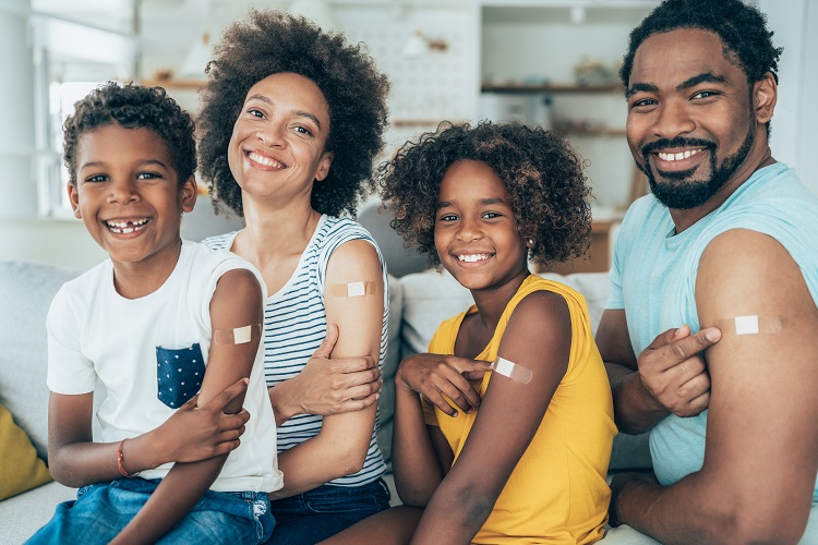 A smiling black family show their left arms which all have a band-aid indicating that they just got vaccinated