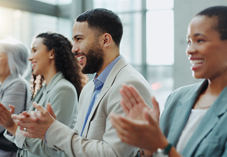 A row of diverse business professionals all smile and applaud while looking off camera