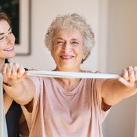 smiling woman stretching a band between her arms for physical activity and wellness while care provider watches and smiles