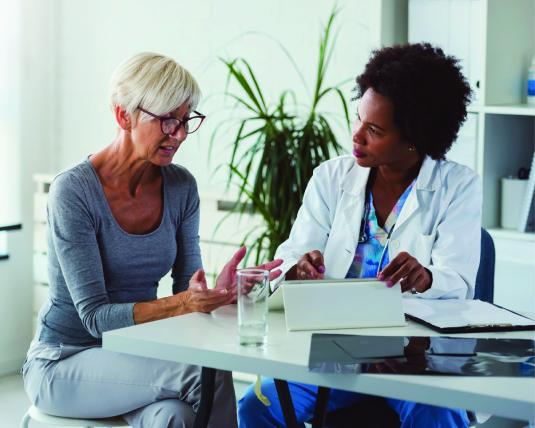 An older woman and her female doctor sit at a table deep in discussion